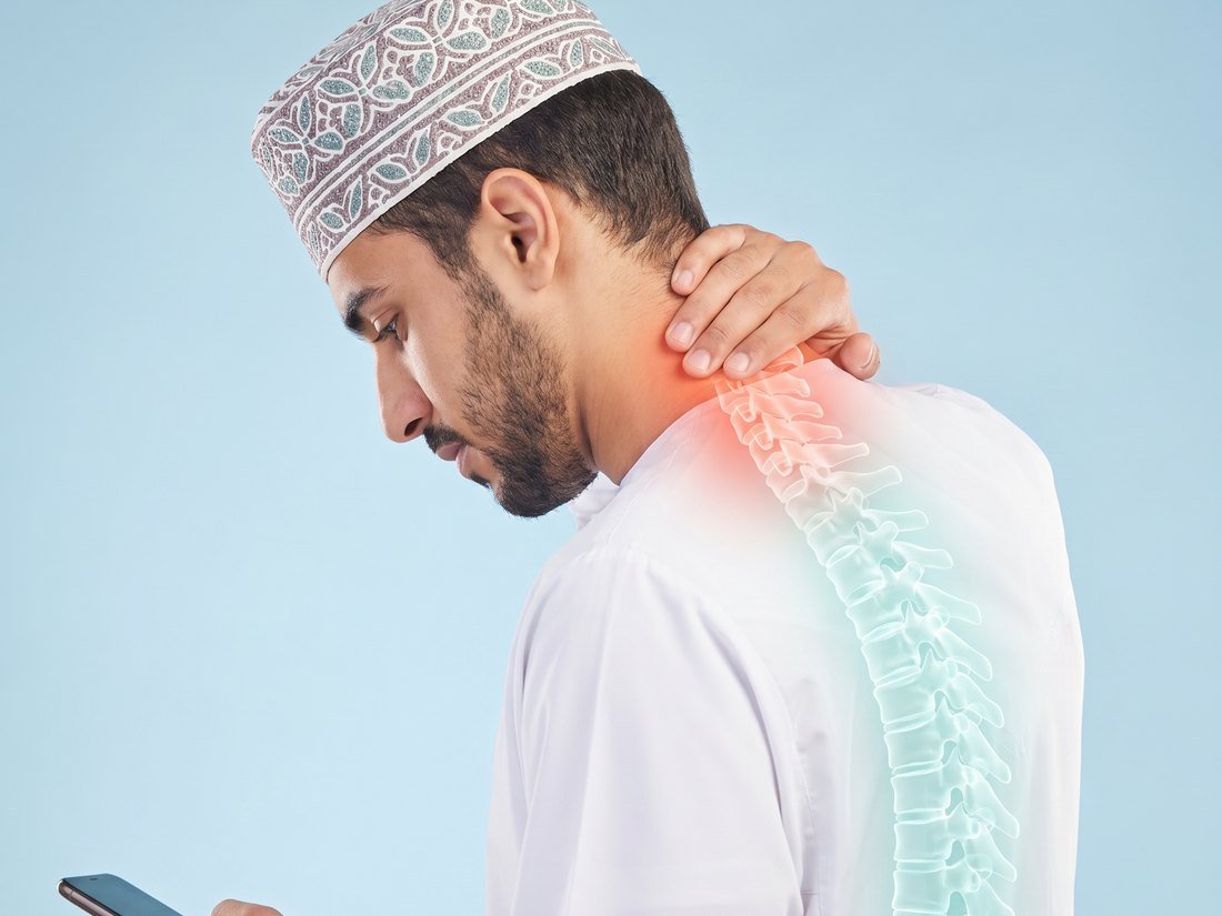 Omani man looking down at a phone with forward-head tech-neck posture and a red glow at the neck
